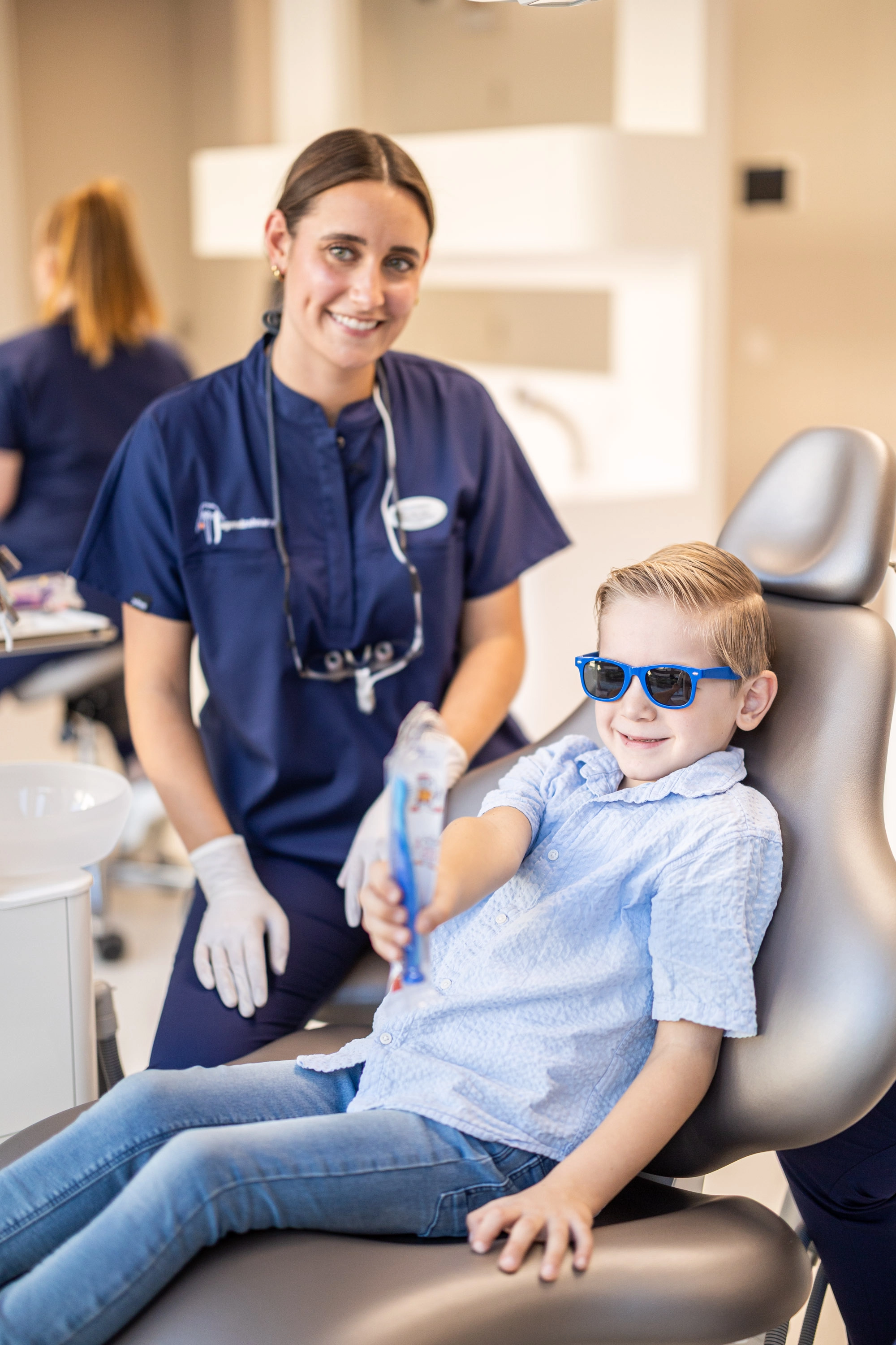 Lächelnde Zahnärztin mit einem fröhlichen Jungen mit Sonnenbrille auf dem Behandlungsstuhl