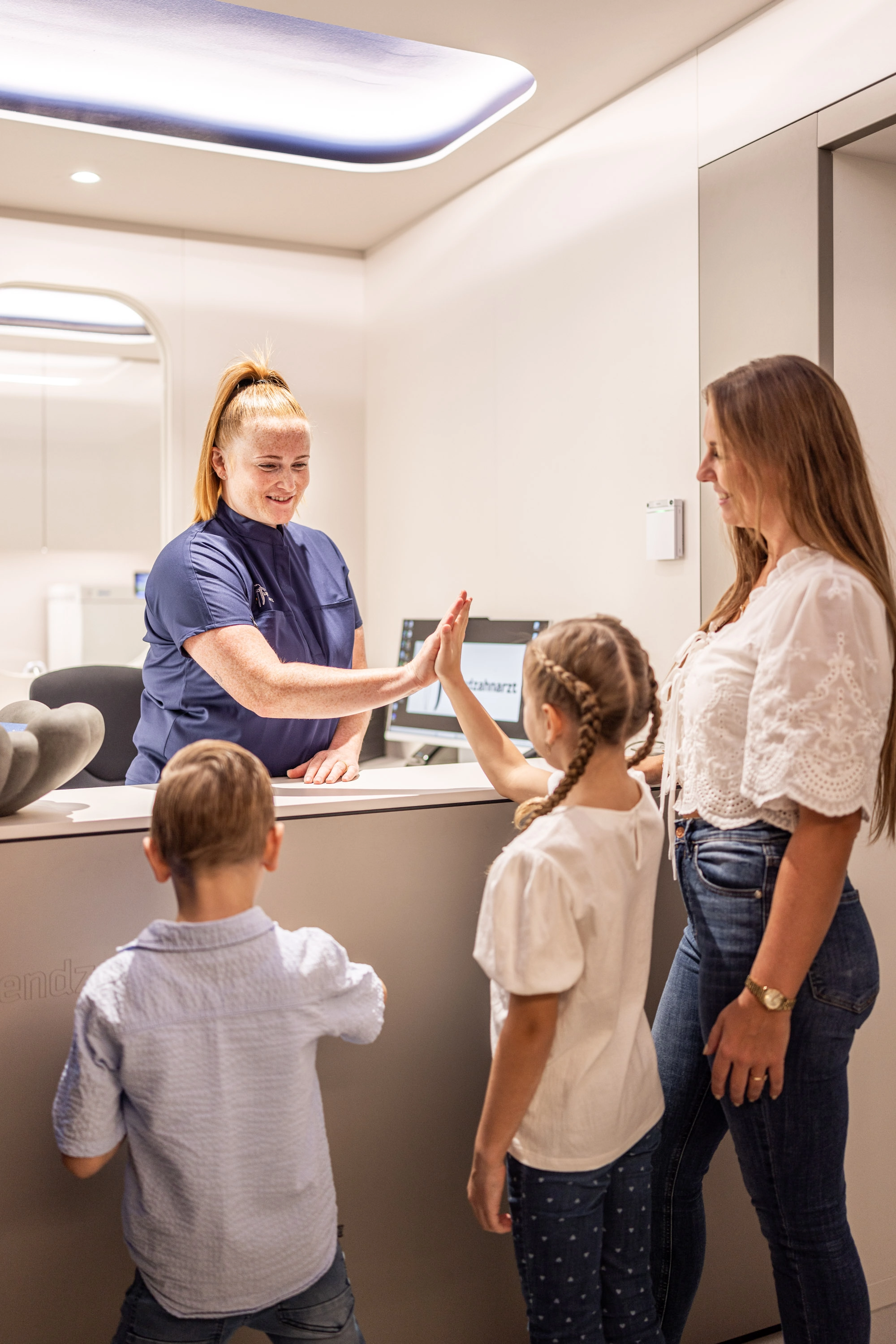 Zahnärztin gibt einem Kind ein High-Five am Empfang während Mutter und Geschwister zusehen