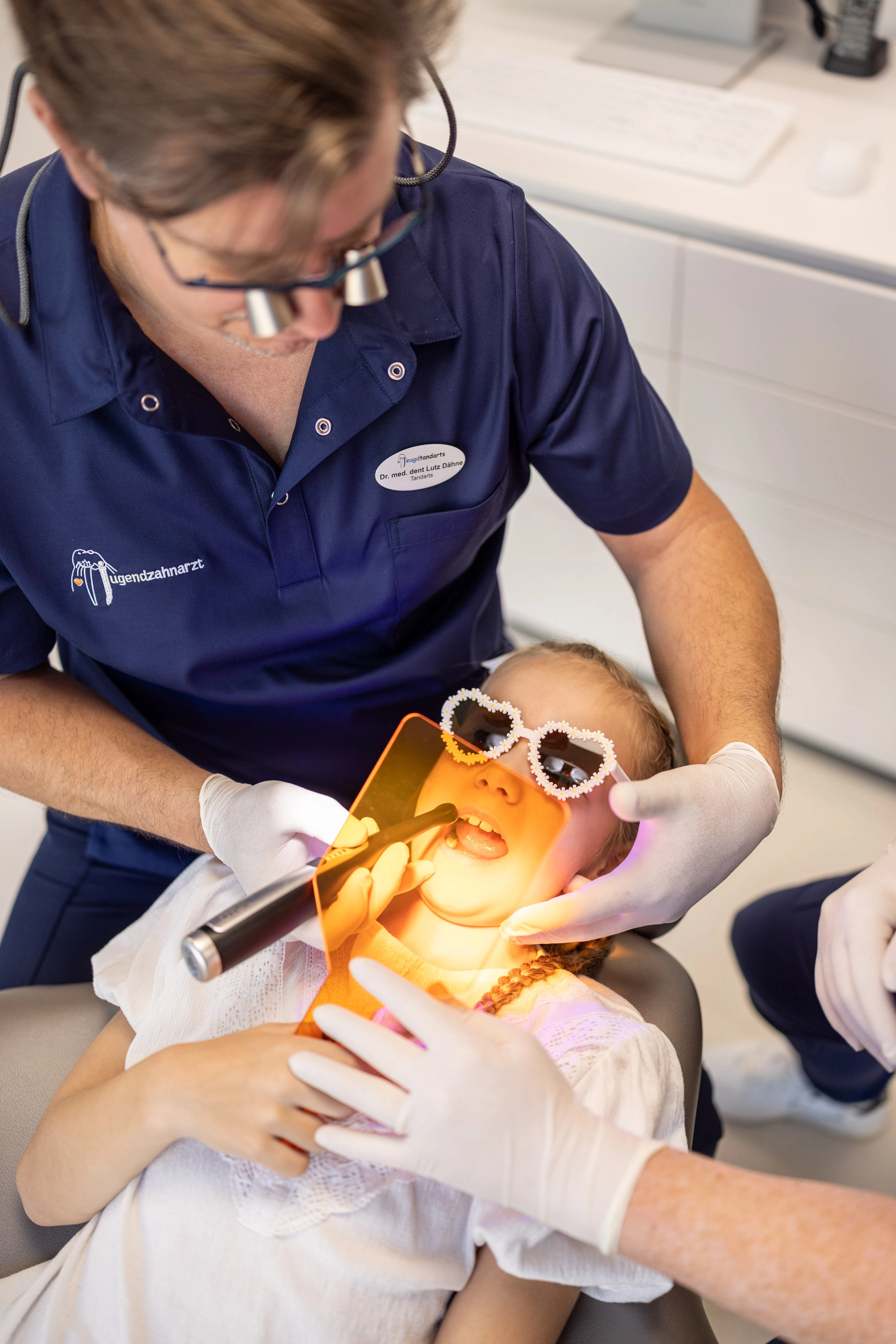 Zahnarzt behandelt ein Kind mit bunter Schutzbrille unter Lichtaushärtung
