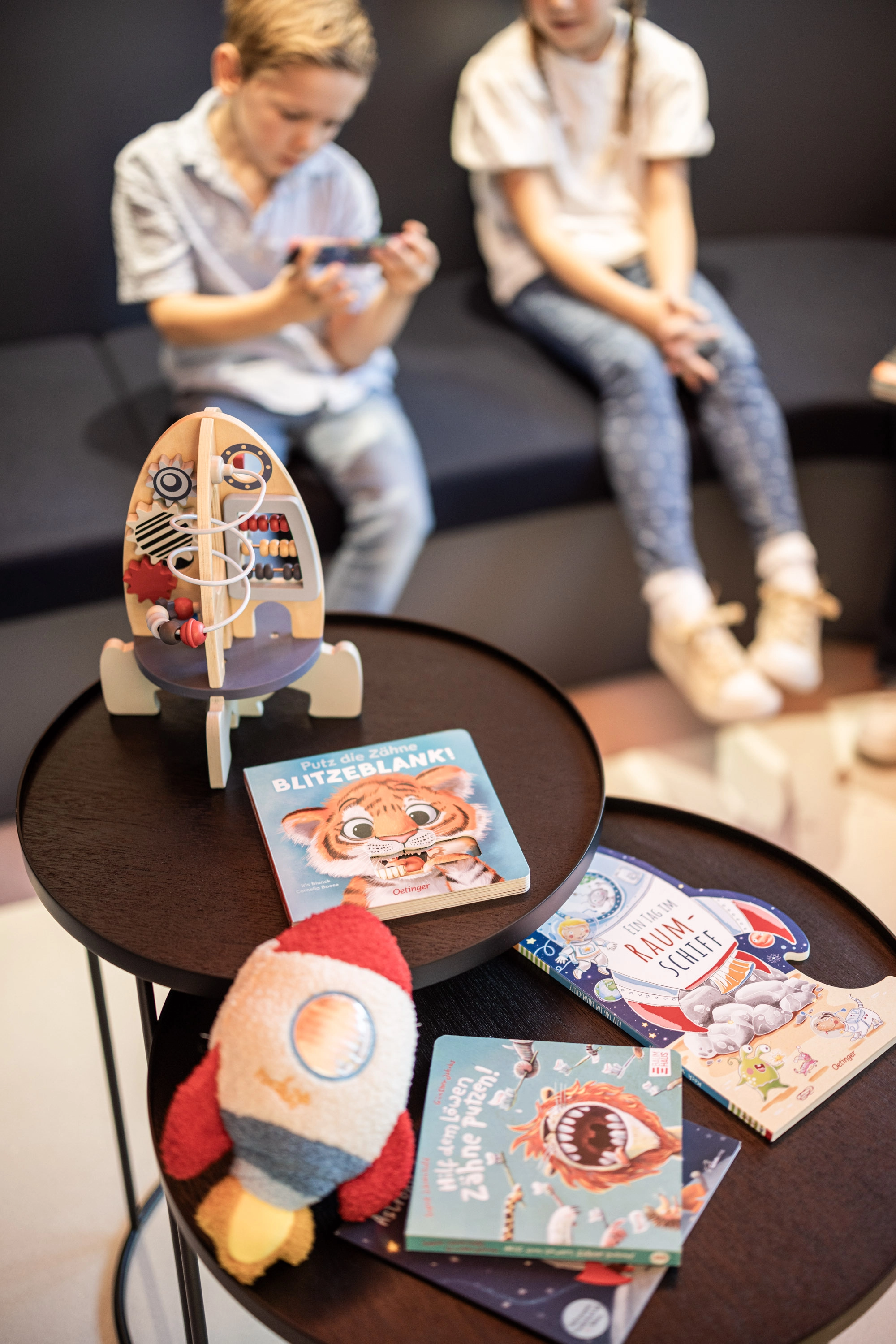 Gemütlicher Wartebereich mit Kinderbüchern, Spielzeug und zwei Kindern auf dem Sofa